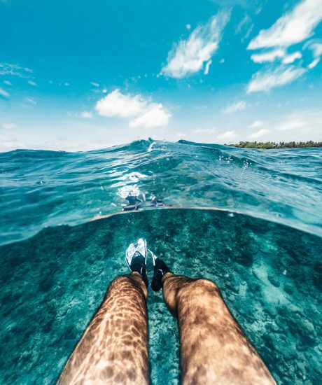 Pov view of man's legs in a clear water - Maldives - Split view hald underwater half overwater